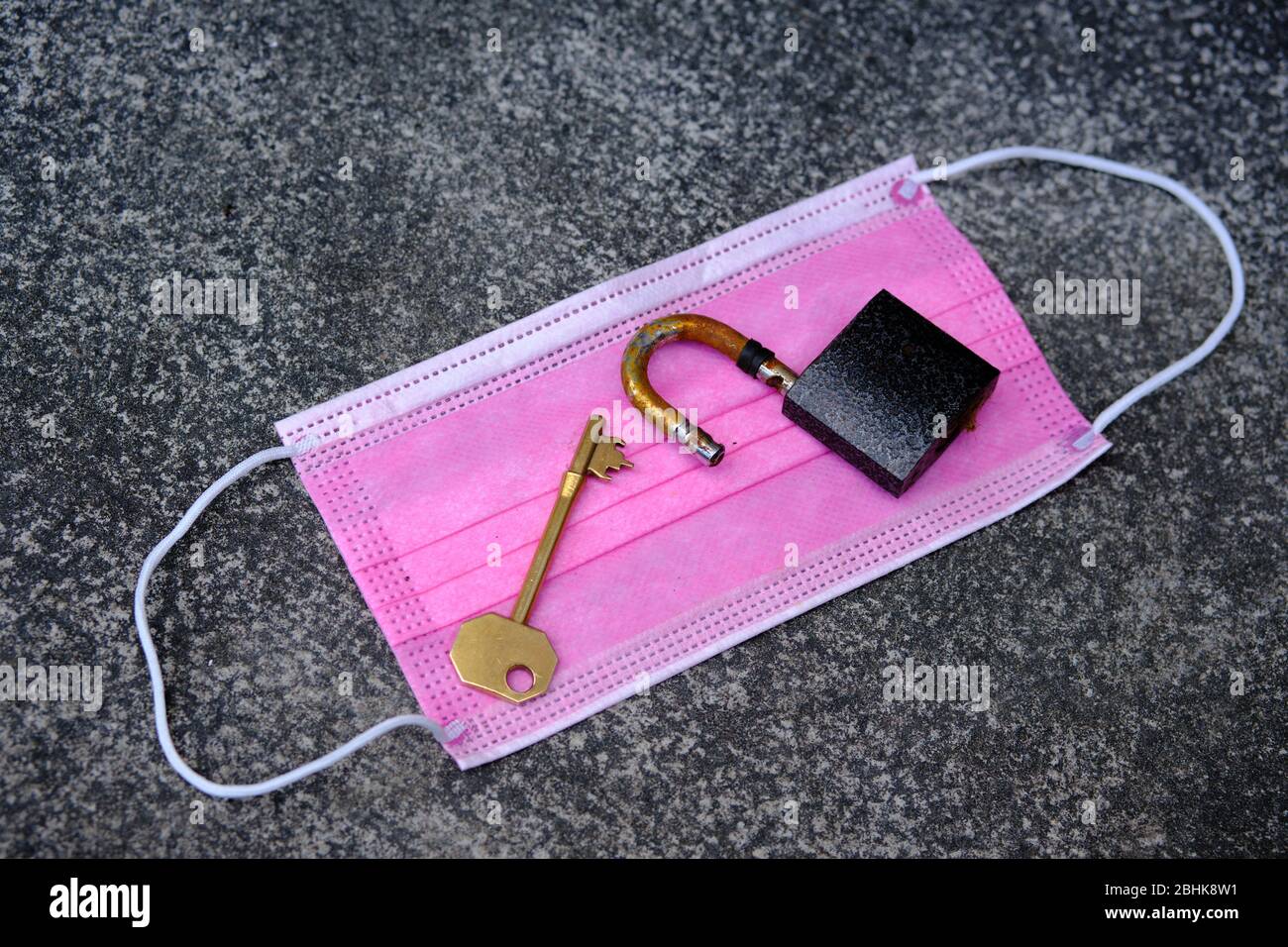 Concetto di blocco Covid-19. Foto di maschera rosa del viso, vecchia serratura e una chiave sopra di essa. Foto Stock