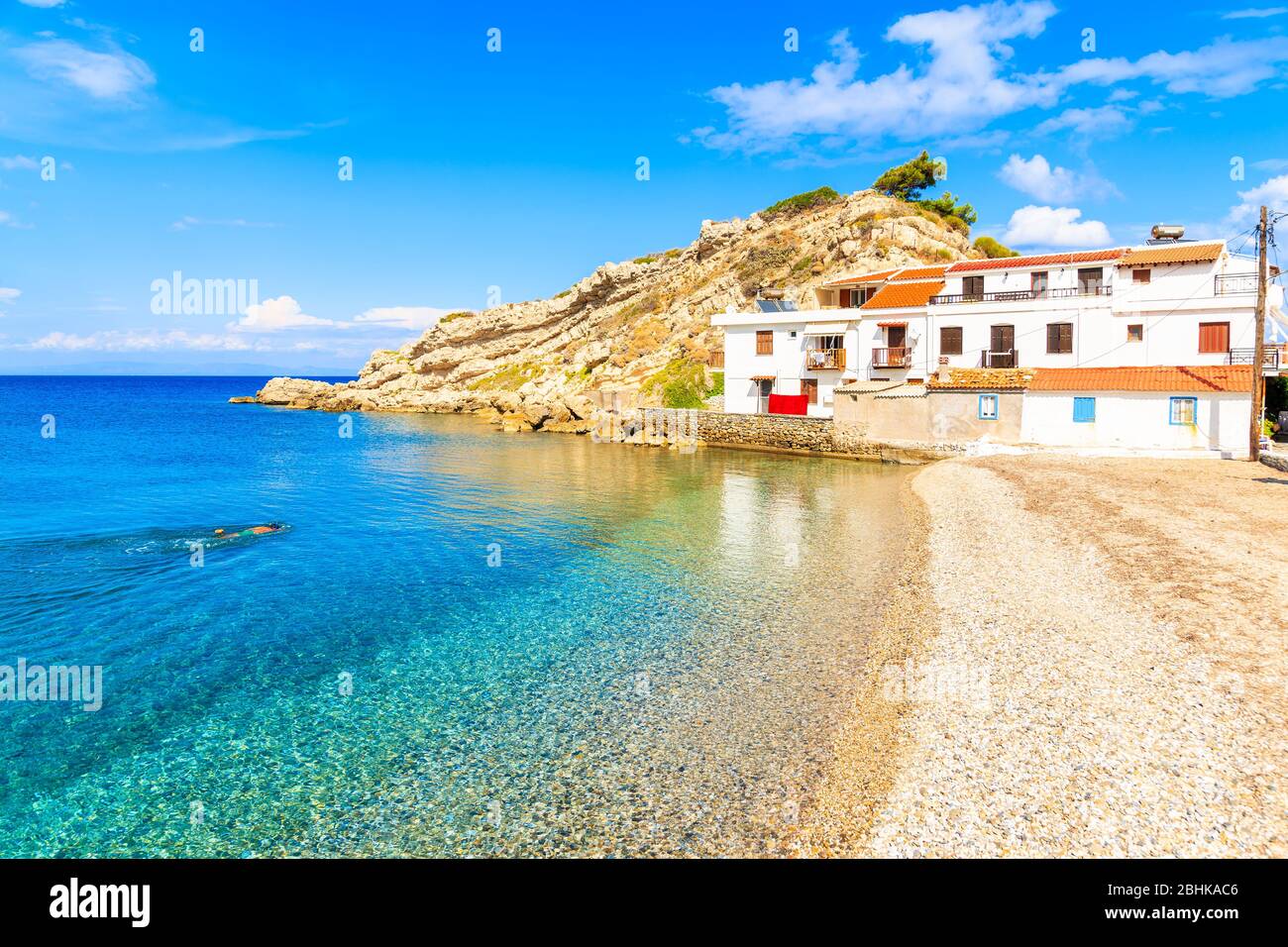 Snorkeling nuotando in acque cristalline azzurre del villaggio di Kokkari con tipiche case bianche sulla riva, isola di Samos, Mar Egeo, Grecia Foto Stock