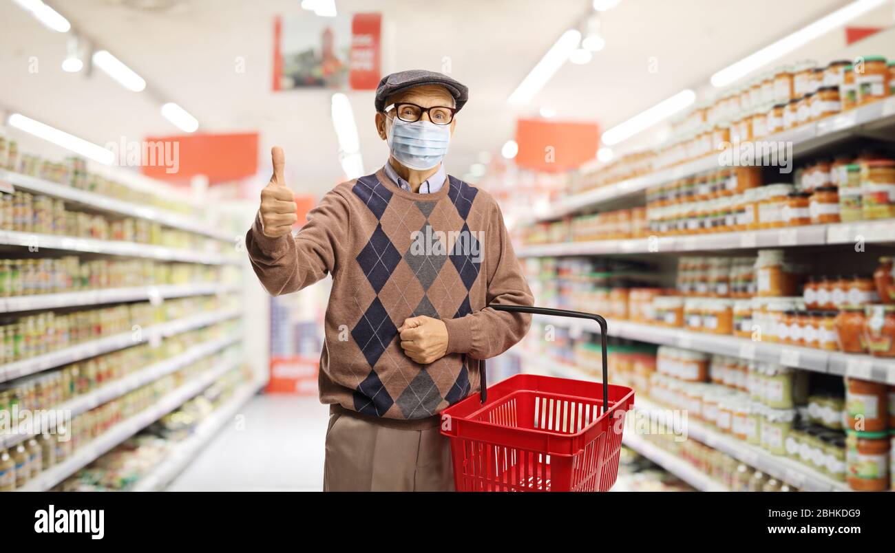 Uomo anziano in un supermercato che indossa una maschera protettiva per il viso e mostra pollici in su Foto Stock