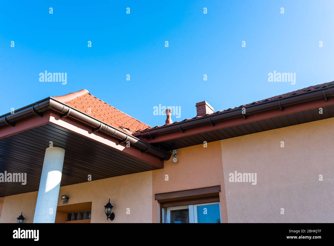 Elevazione dell'edificio in color salmone con una colonna di cemento, soffit in legno e telecamere di sicurezza sulla parete. Foto Stock