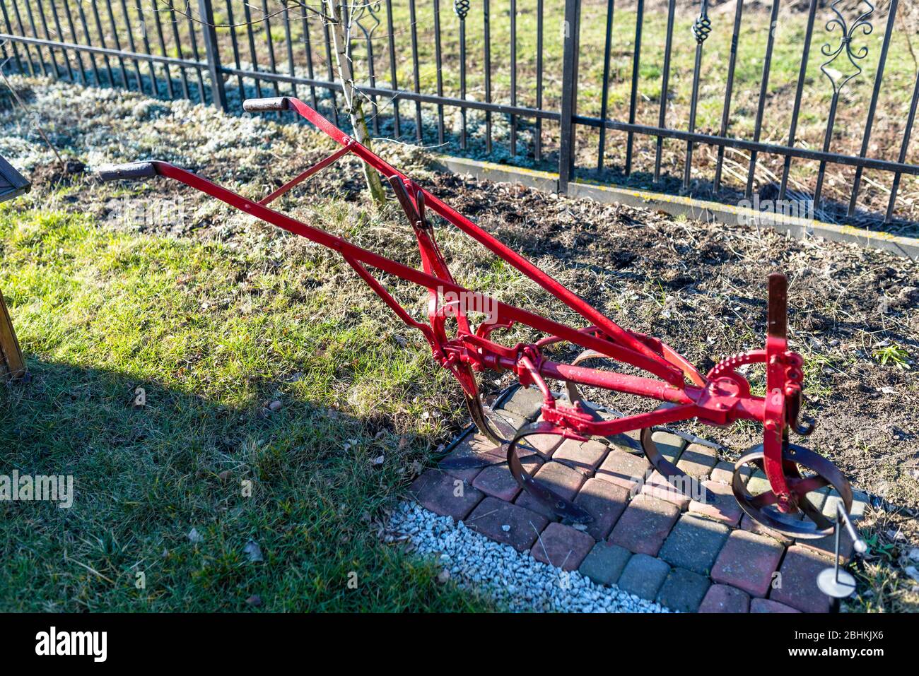 Tradizionale aratro manuale rosso in acciaio, in piedi nel giardino come ornamento. Foto Stock
