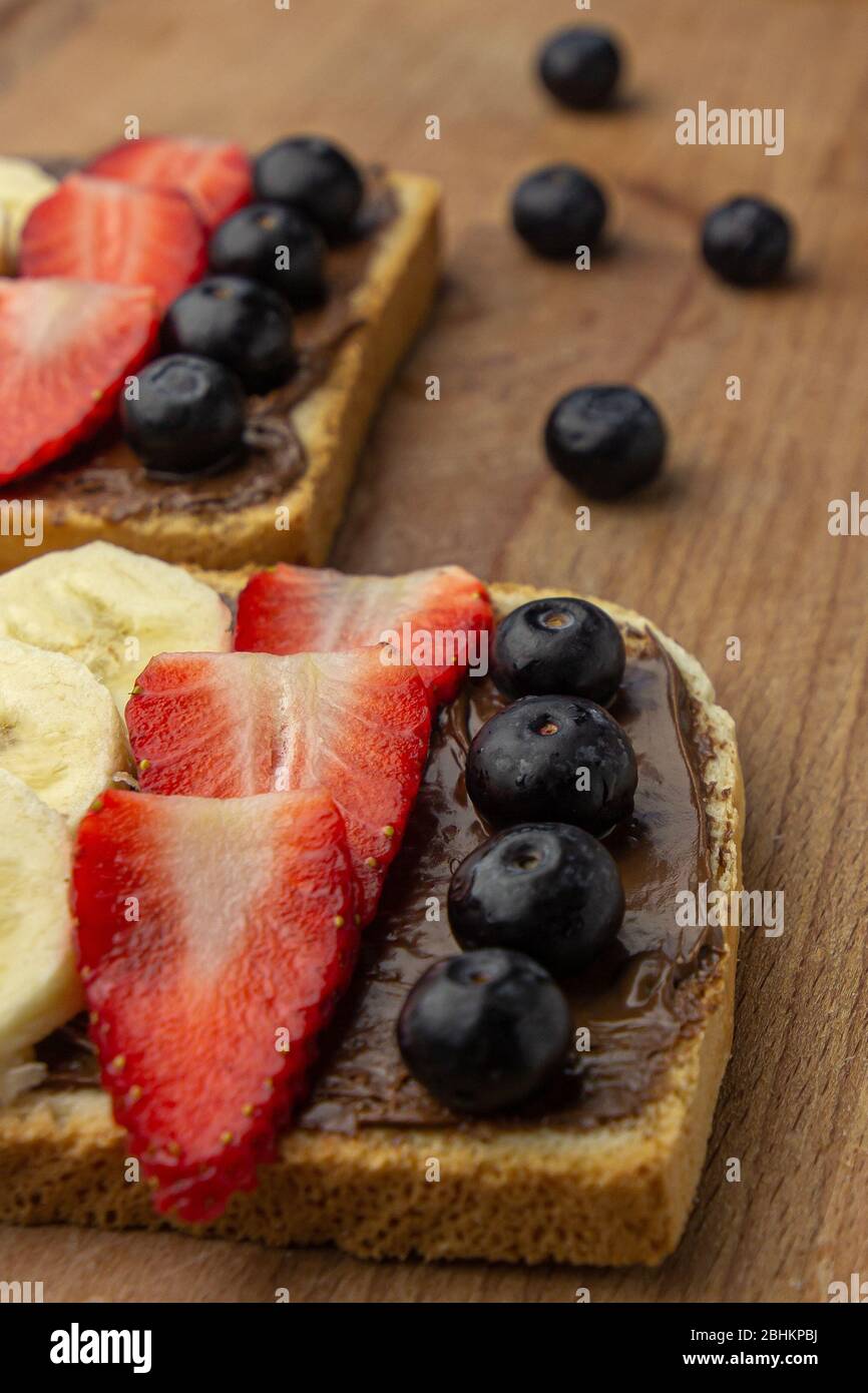 Colazione con panino di frutta con fragola, banana, mirtillo su un asse di legno. Concetto di pasto sano. Foto Stock
