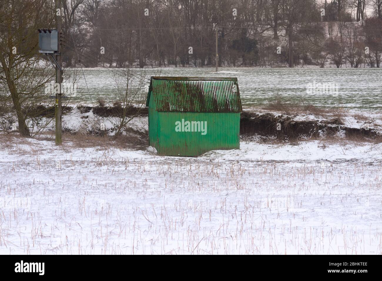 Un vecchio capanno di metallo corugato dipinto di verde si trova in un campo agricolo coperto da una neve leggera. Foto Stock