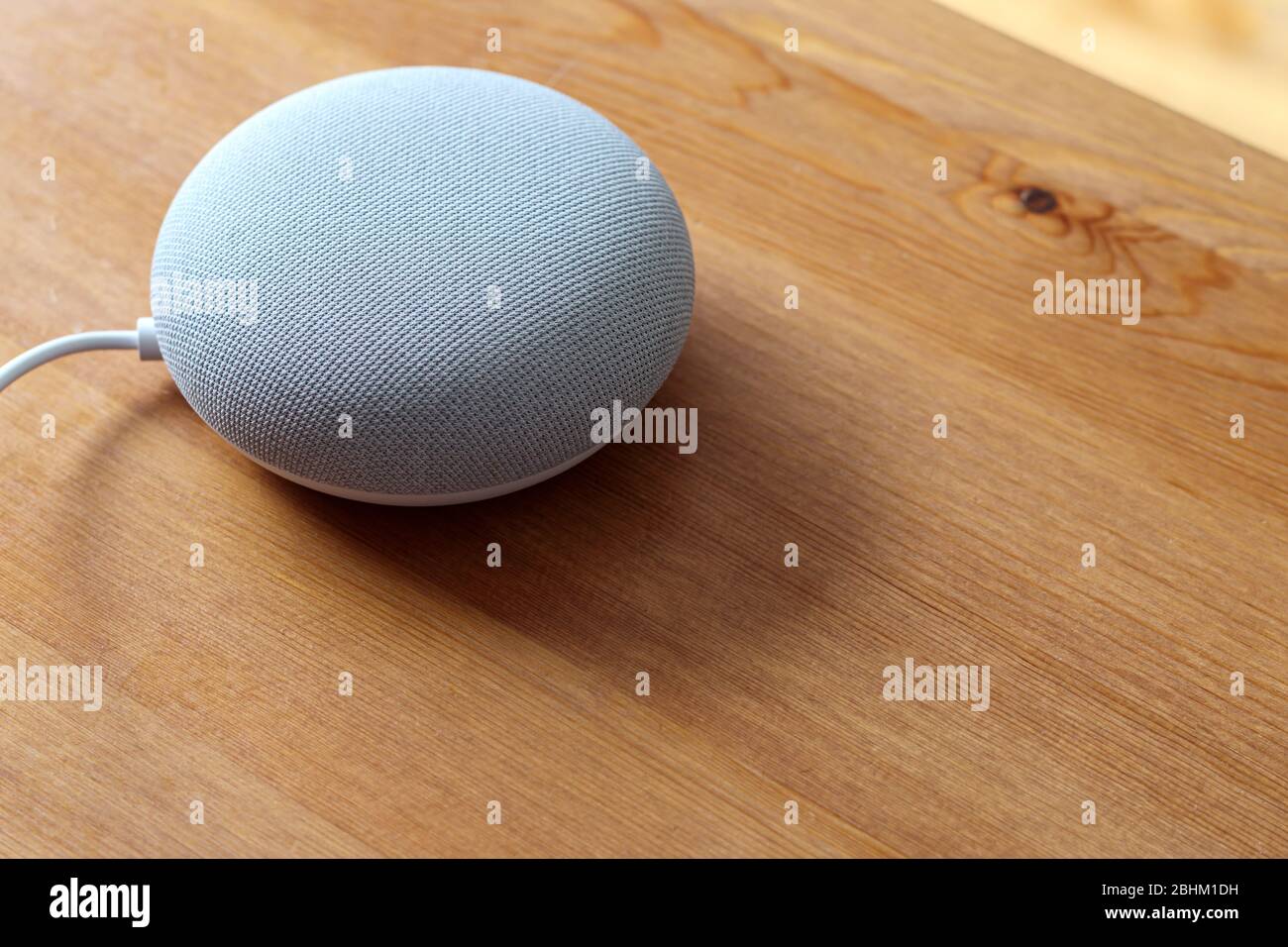 Un altoparlante intelligente Google Nest Mini si trova su un tavolo di legno Foto Stock