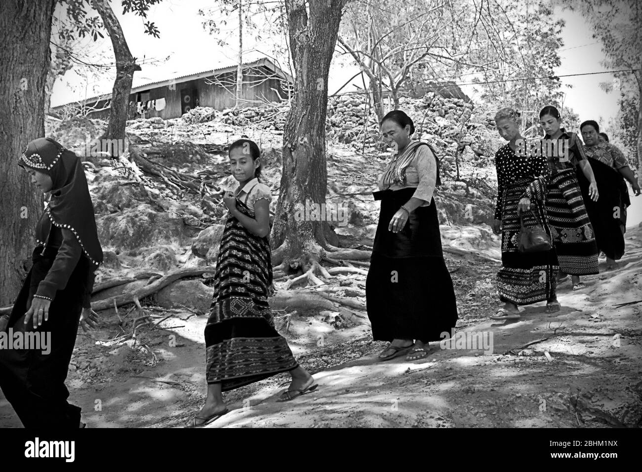 Le donne che camminano su un percorso rurale per partecipare ad una sessione di lutto come un membro della loro comunità è passato via a Kilimbatu, Kawangu, Pandawai, Sumba orientale, Nusa Tenggara orientale, Indonesia. La tradizione legata alla morte nelle comunità Sumbanesi richiede un invito da parte della famiglia in lutto per quanto riguarda chi dovrebbe venire all'evento. Foto Stock