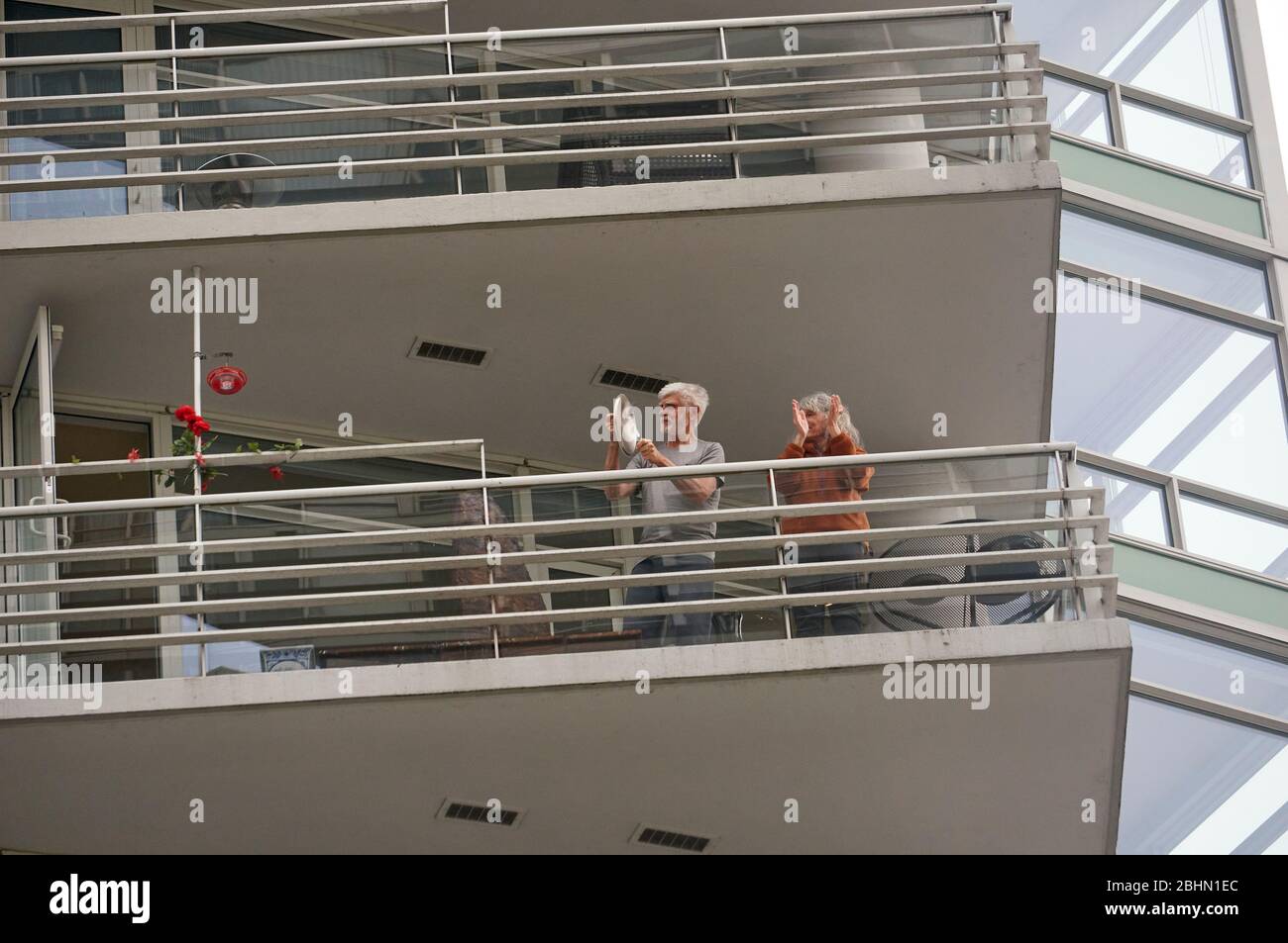 Vancouver, Canada, 26 aprile 2020. Un uomo e una donna che si trova sul balcone del loro edificio di appartamenti bang pentole e padelle da cucina insieme e si aggrappano per mostrare il supporto per gli operatori sanitari durante la pandemia COVD-19. Foto Stock