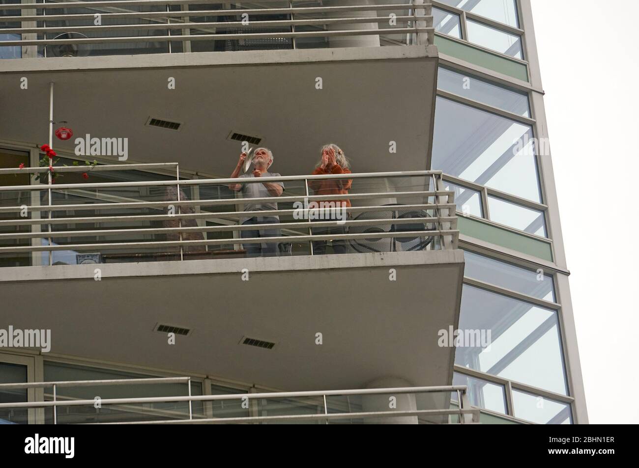 Vancouver, Canada, 26 aprile 2020. Un uomo e una donna che si trova sul balcone del loro edificio di appartamenti bang pentole e padelle da cucina insieme e si aggrappano per mostrare il supporto per gli operatori sanitari durante la pandemia COVD-19. Foto Stock