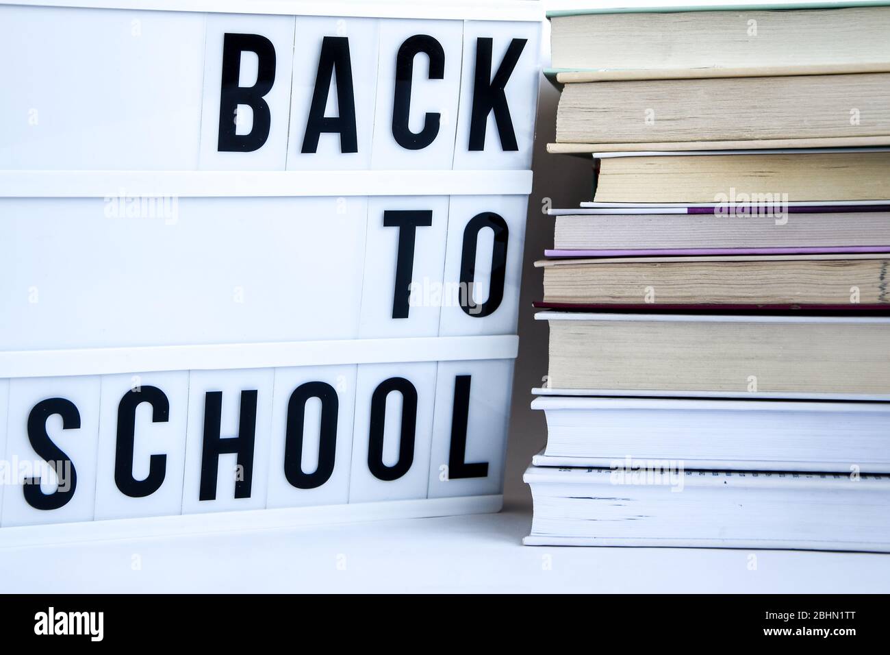 Scatola luminosa con testo DI RITORNO A SCUOLA e libri su sfondo bianco Foto Stock