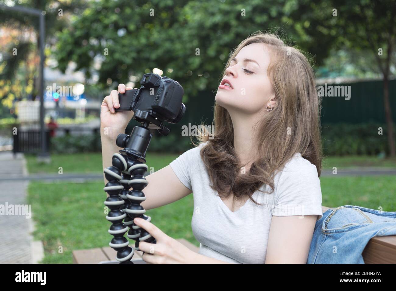 Sorridente giovane donna caucasica ragazza facendo un video blog (vlog) con fotocamera all'esterno in parco verde Foto Stock