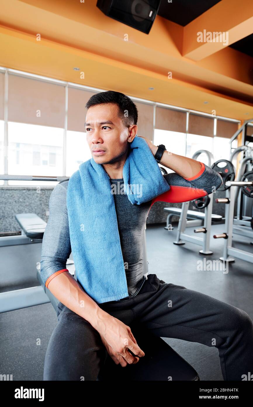 Stanco sportivo asiatico spazzando il sudore dal collo dopo aver fatto esercizio di pressione in palestra Foto Stock