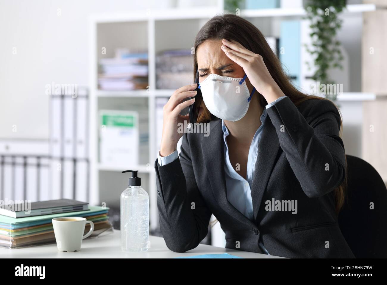 Donna executive con chiamate di mal di testa su smartphone con maschera protettiva Foto Stock