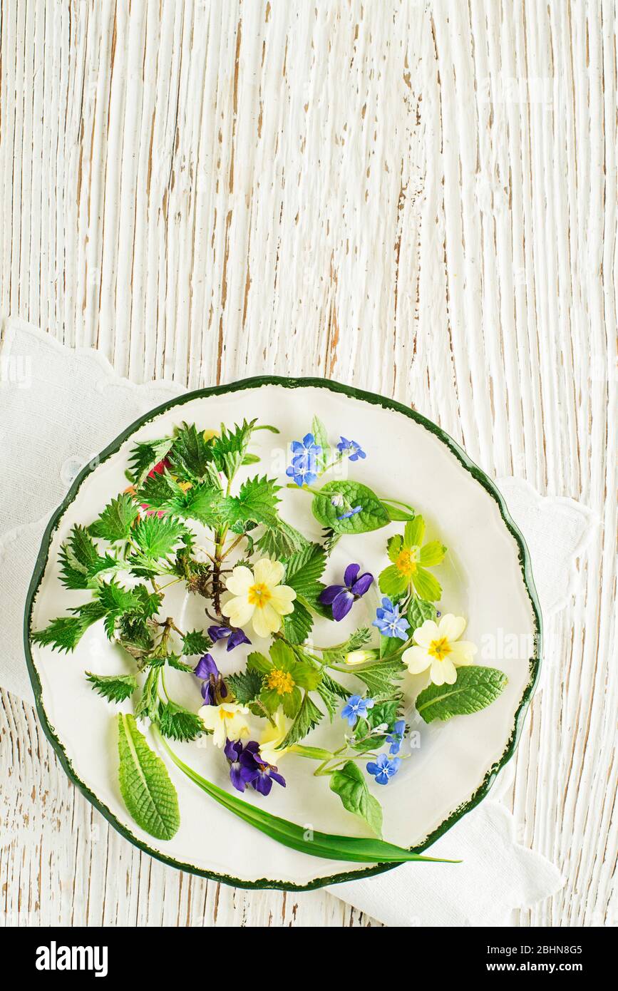 Ingredienti sani per gli alimenti primaverili. Dente di leone, fiori, aglio selvatico e ortica su sfondo di legno Foto Stock