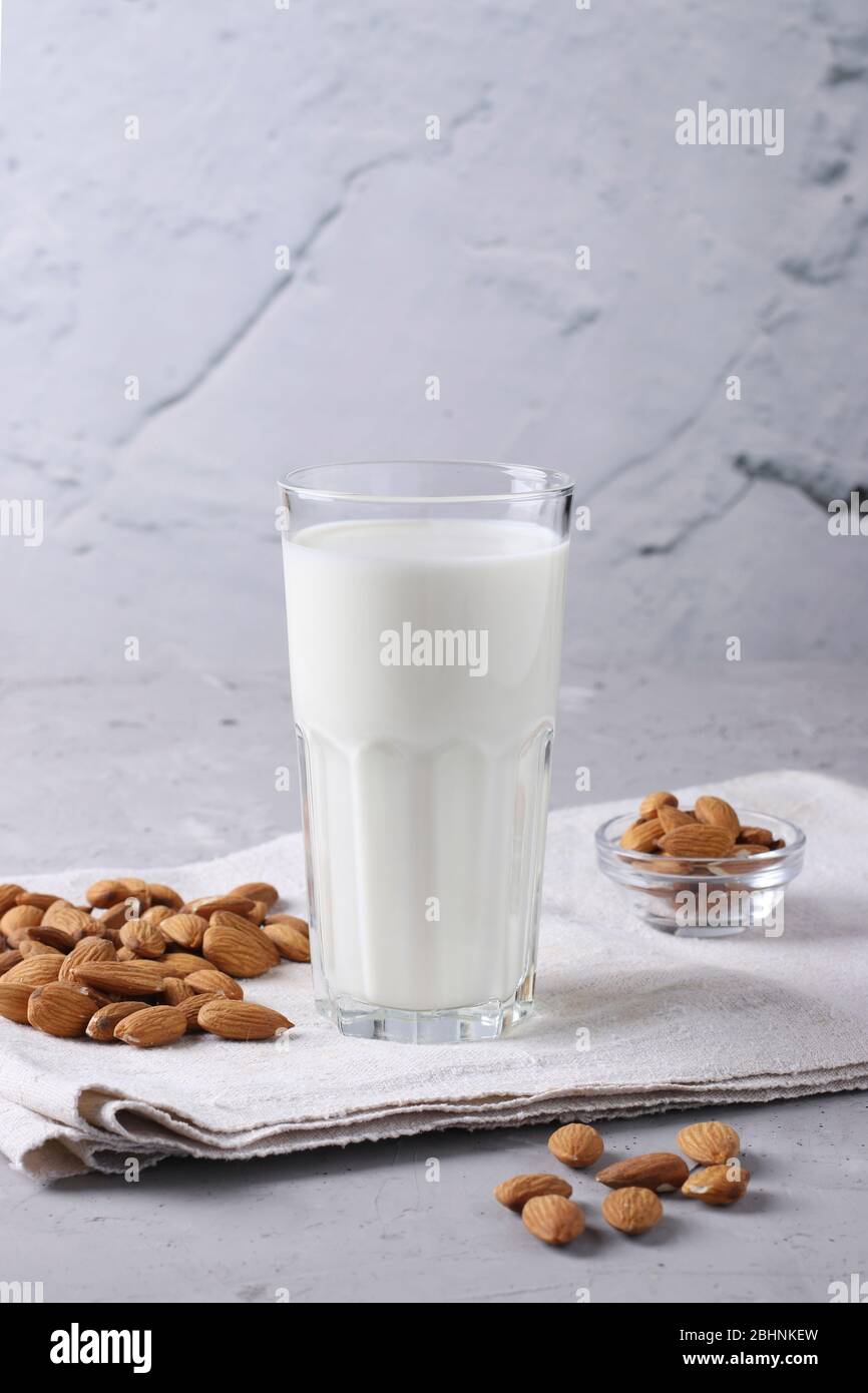 Latte fresco di mandorle in vetro trasparente e mandorle su fondo grigio cemento, salutare sostituto del latte vegano, formato verticale, Closeup Foto Stock