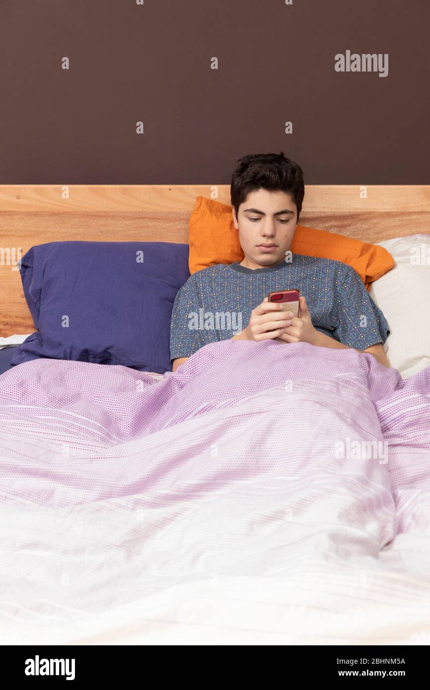 Ragazzo a letto con il telefono, perde solo tempo e forse chiacchiera o  guarda qualcosa. Posizione anteriore Foto stock - Alamy