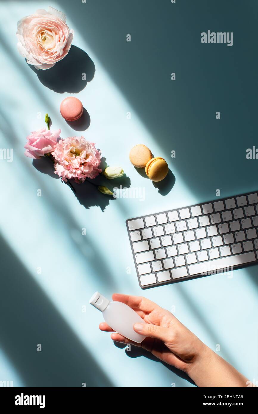 Fiat piatto con fiori e macaroon alla luce del sole e con un igienizzante su una mano femminile. Igiene e misure preventive sul posto di lavoro. Foto Stock