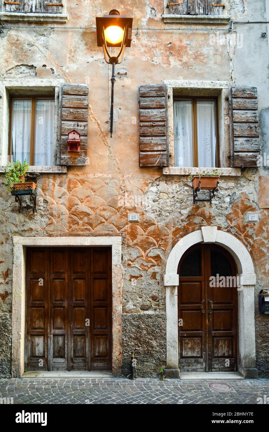 façade di una vecchia casa nel centro storico con porte e persiane in legno e pareti cracked decorate con motivi a scala di pesce, Bardolino, Italia Foto Stock