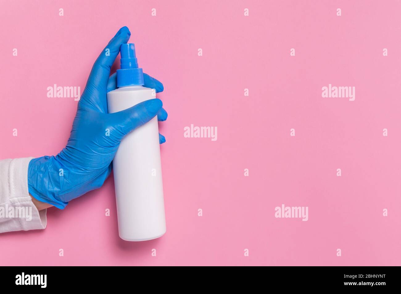 Protezione da coronavirus. Guanti monouso blu con flacone spray di disinfettante per superfici o dispenser di igienizzante per mani su sfondo rosa. Ig Foto Stock