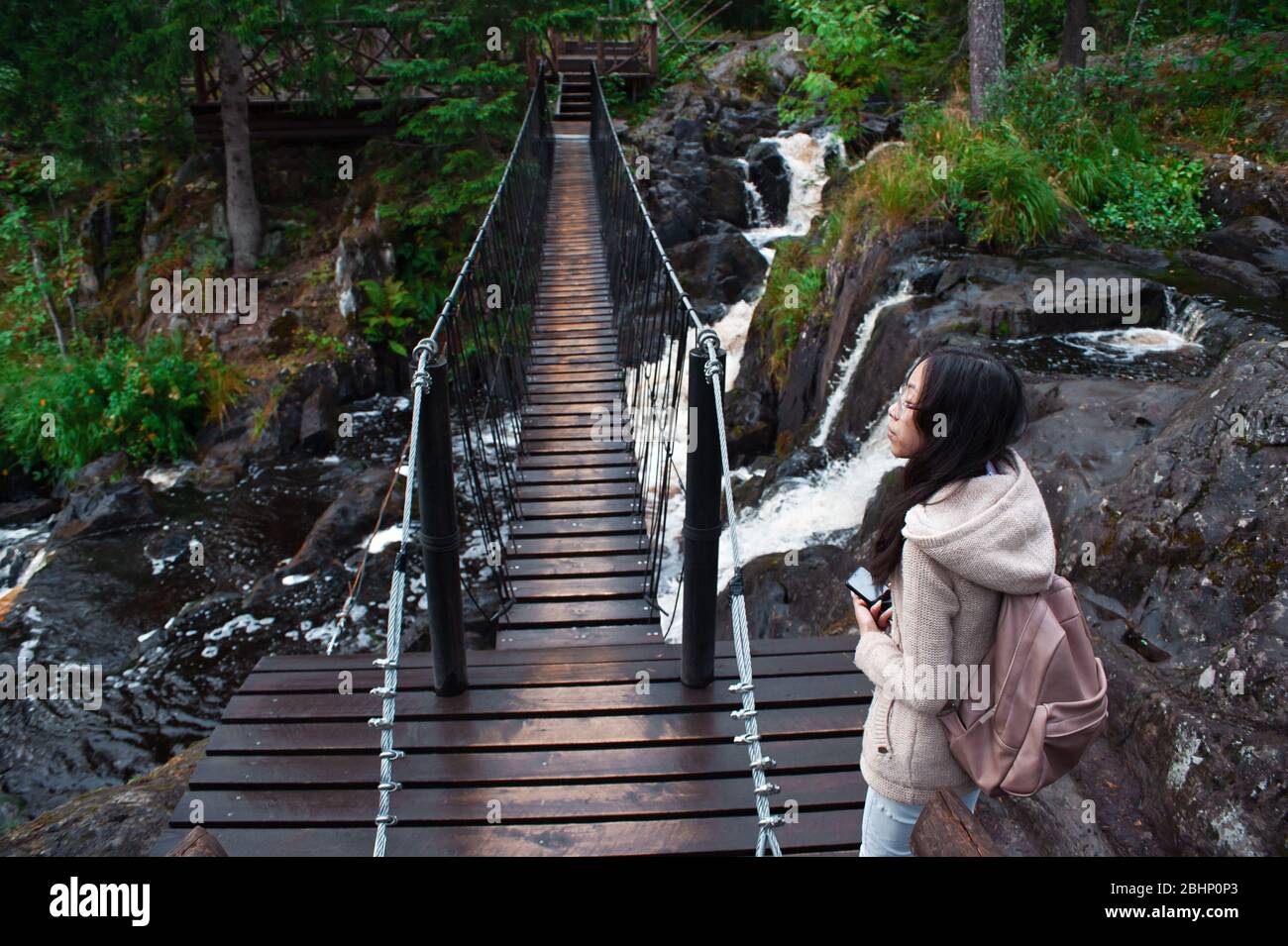 Solitaria giovane donna turistica va su un ponte sospeso nella foresta Foto Stock