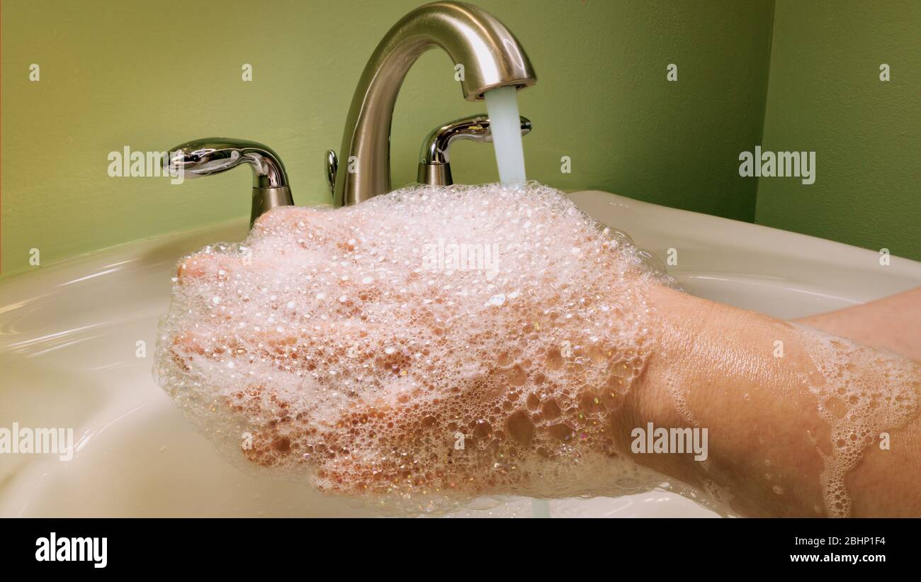 Donna lavando le mani con acqua e sapone in un bagno verde durante la quarantena del coronavirus. Foto Stock