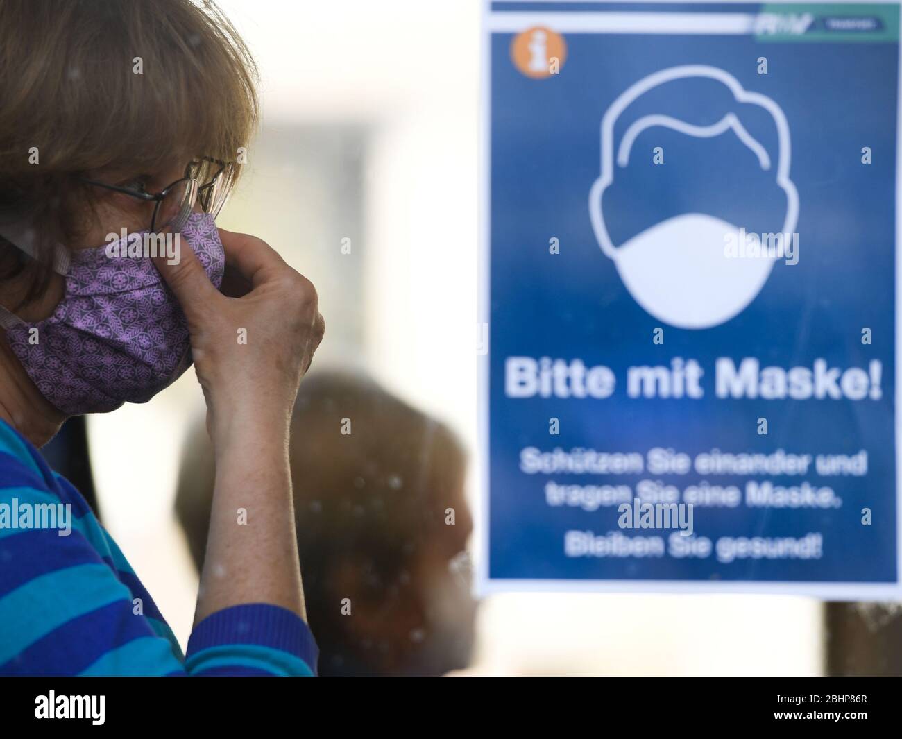 27 aprile 2020, Hessen, Francoforte sul meno: Una donna con maschera facciale si sposta alla fermata Konstabler Wache in un autobus accanto ad un poster con l'iscrizione 'Bitte mit Maske! Proteggersi e indossare una maschera. Rimanere in salute!" raddrizza la maschera. Foto: Arne Dedert/dpa Foto Stock