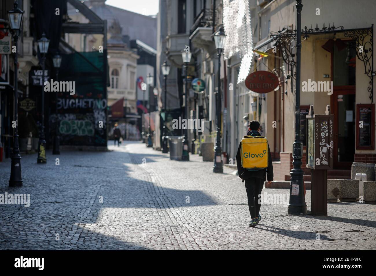 Bucarest, Romania - 22 aprile 2020: Uomo che trasporta uno zaino di consegna Glovo sulle strade vuote della città vecchia di Bucarest durante il convid-19 di chiusura. Foto Stock