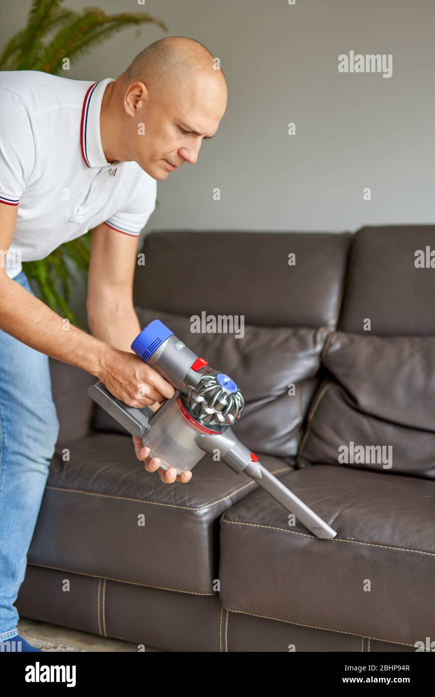 Divano uomo per la pulizia con aspirapolvere manuale mentre lavori nel soggiorno. Servizio di pulizia. Lavori domestici Foto Stock