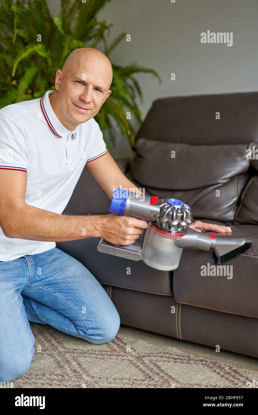 Divano uomo per la pulizia con aspirapolvere manuale mentre lavori nel soggiorno. Servizio di pulizia. Lavori domestici Foto Stock