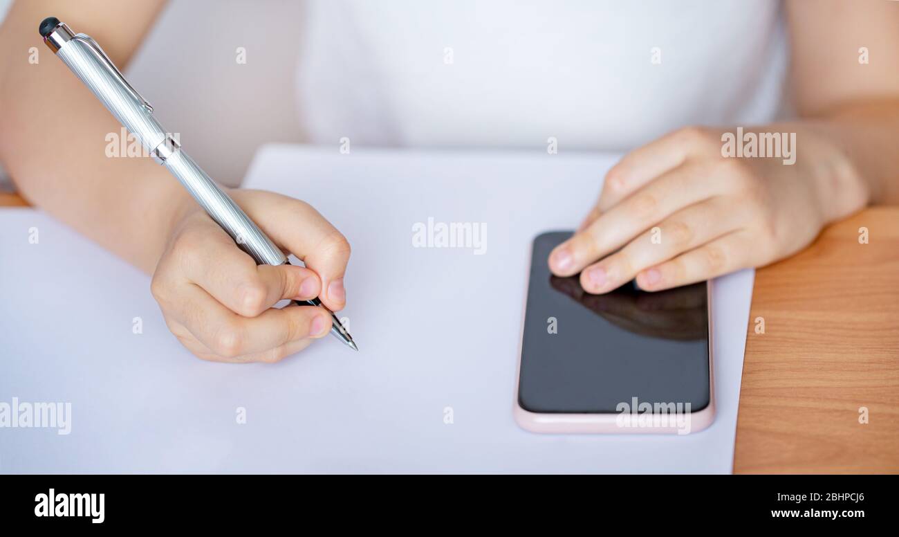 Il bambino scrive in un notebook e guarda il telefono. Apprendimento a distanza. Primo piano. Foto Stock