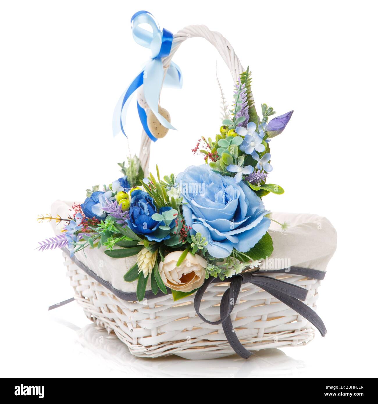 Decorazioni floreali pasquali in blu su un cesto bianco in vimini su sfondo bianco Foto Stock