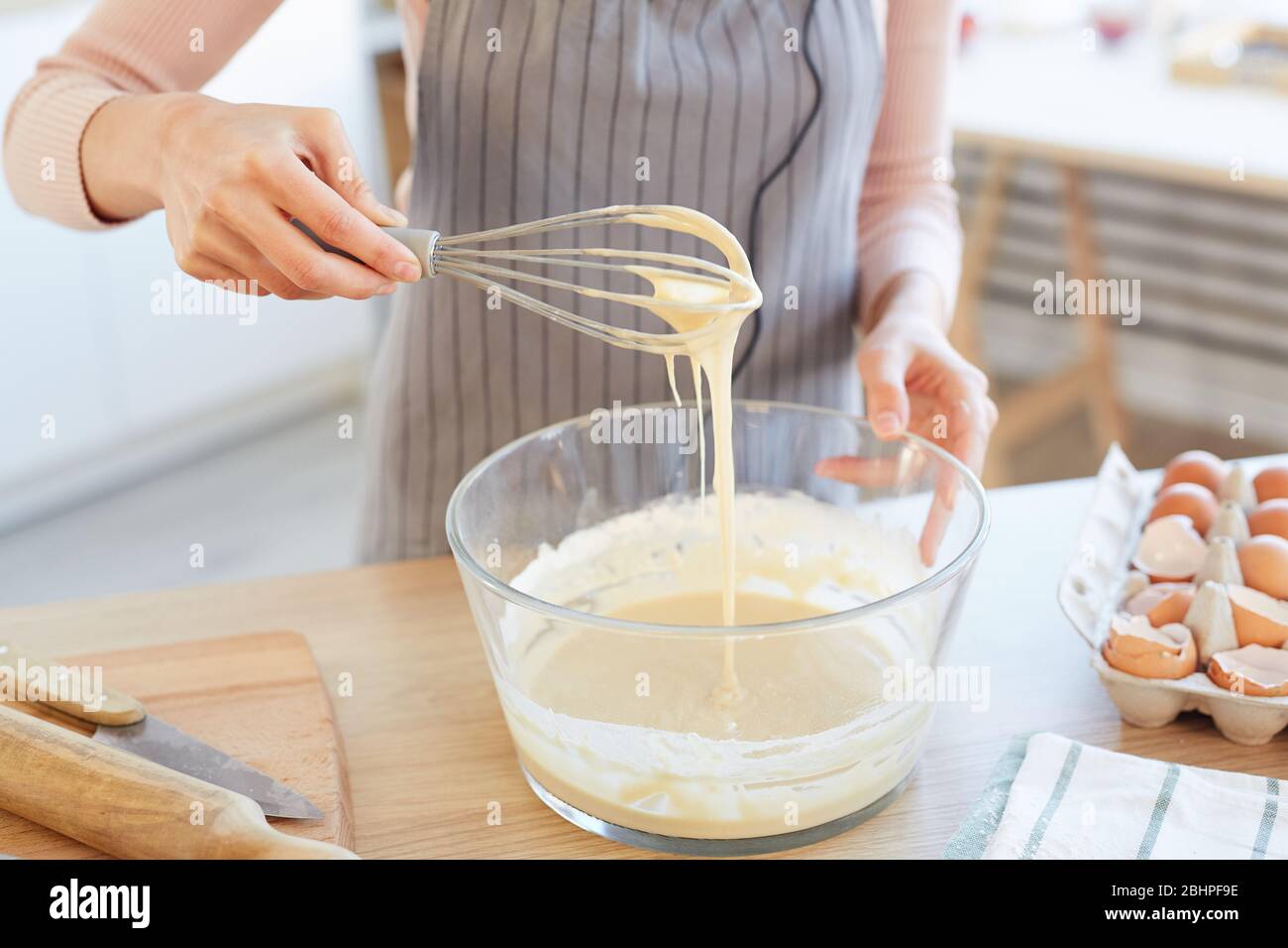 Donna irriconoscibile che fa l'impasto per i cupcake usando frusta, colpo orizzontale ad angolo alto Foto Stock