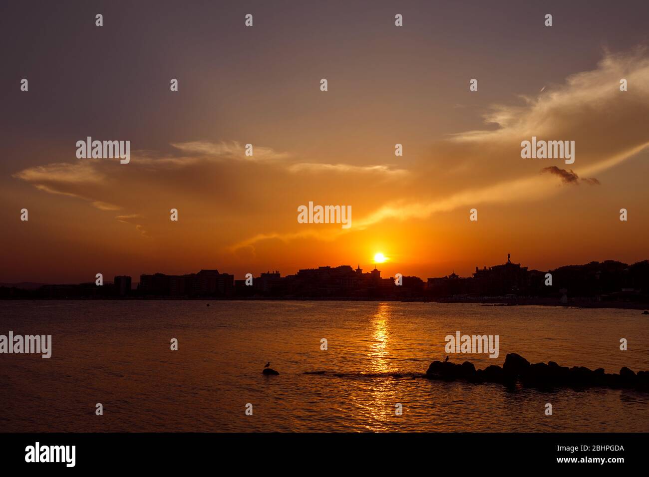 Tramonto sulla città. Silhouette della città al mare. Cielo drammatico. Foto Stock