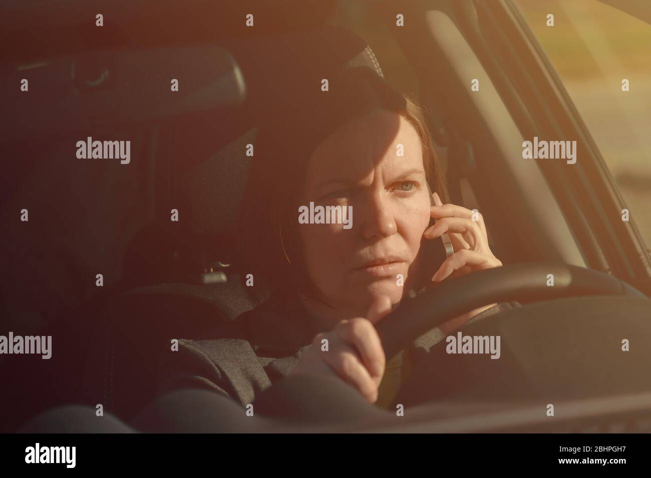 Donna d'affari che parla sul telefono cellulare in auto mentre si guida al lavoro, fuoco selettivo Foto Stock