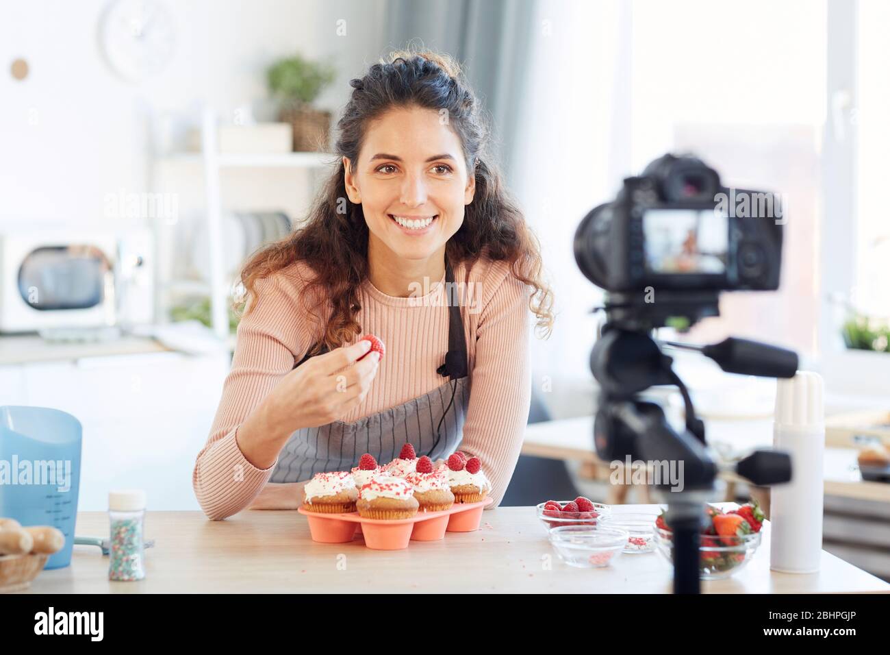 Giovane donna allegra con grembiule degustazione di fragola dolce sulla macchina fotografica, ritratto orizzontale Foto Stock