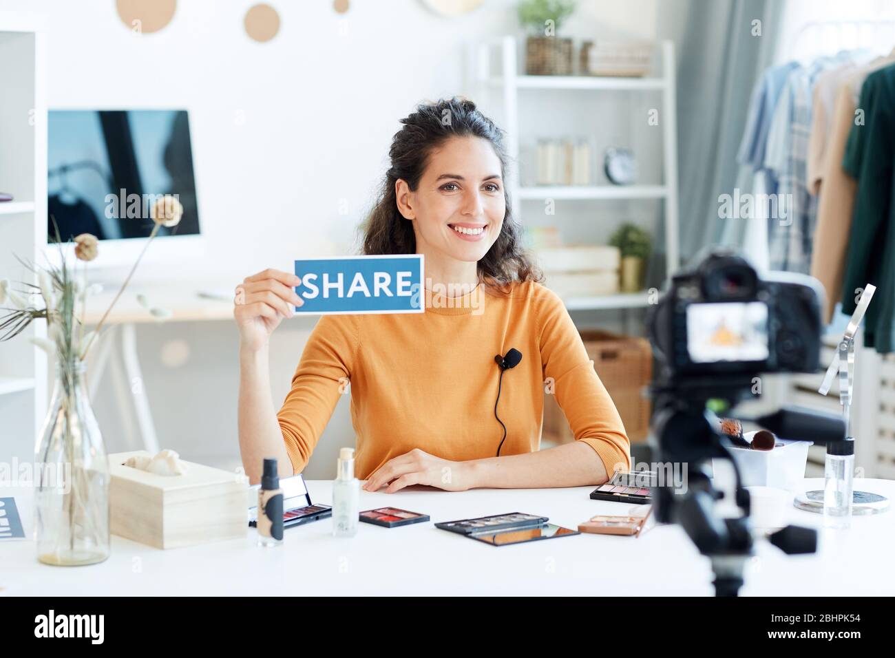 Attraente giovane adulto blogger di bellezza seduto al tavolo tenendo Condividi segno di stampa, ritratto orizzontale girato Foto Stock