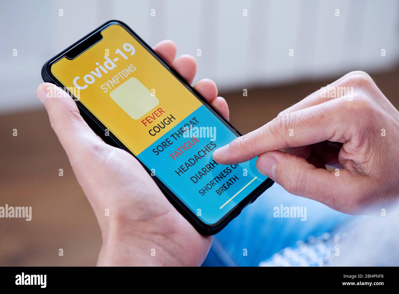 primo piano di un giovane caucasico, seduto comodamente in poltrona, controllando alcuni dei sintomi del covid-19 in una app simulata nel suo smartpho Foto Stock