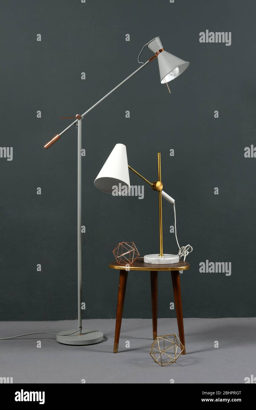 Due lampade ad anglepoise d'epoca, una da pavimento indipendente e la seconda da tavolo su uno sgabello, contro una parete grigia all'interno Foto Stock