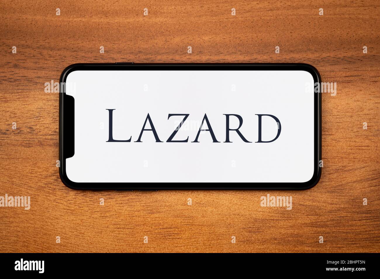 Uno smartphone con il logo Lazard è appoggiato su un tavolo di legno (solo per uso editoriale). Foto Stock
