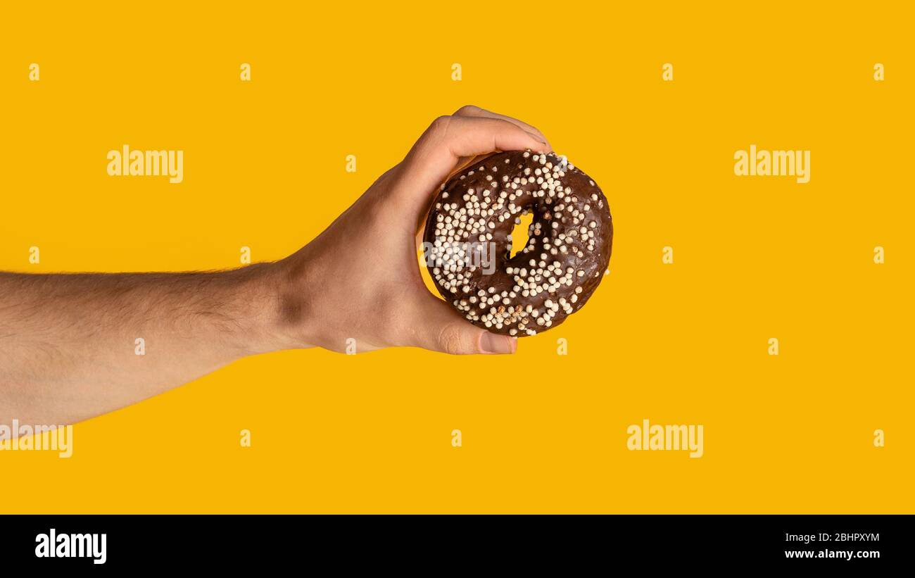 Primo piano della mano maschile mostrando ciambella di cioccolato dolce su sfondo arancione, spazio copia. Panorama Foto Stock
