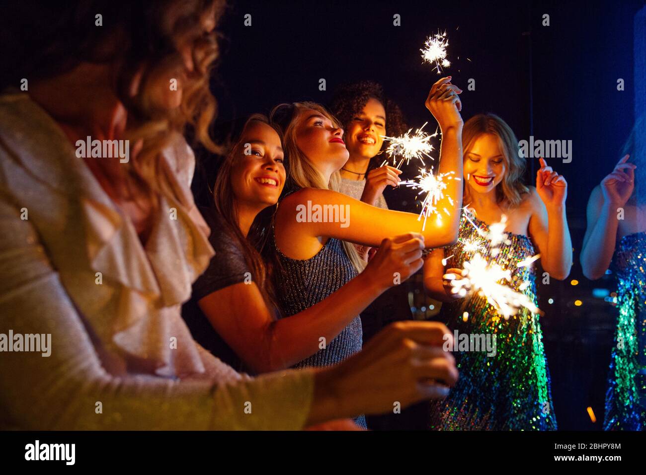 Cinque donne vestite per uscire per la sera in piedi fuori con i luccicanti. Foto Stock