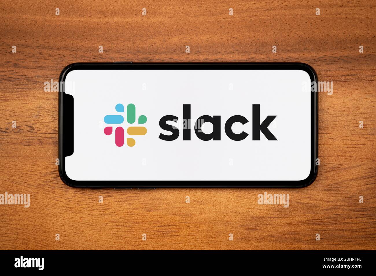 Uno smartphone con il logo slack si appoggia su un tavolo di legno (solo per uso editoriale). Foto Stock