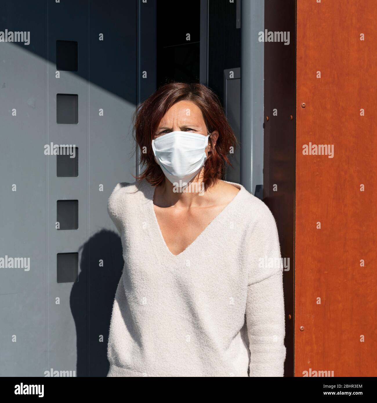 Donna che indossa la maschera a casa, di fronte alla porta Foto Stock