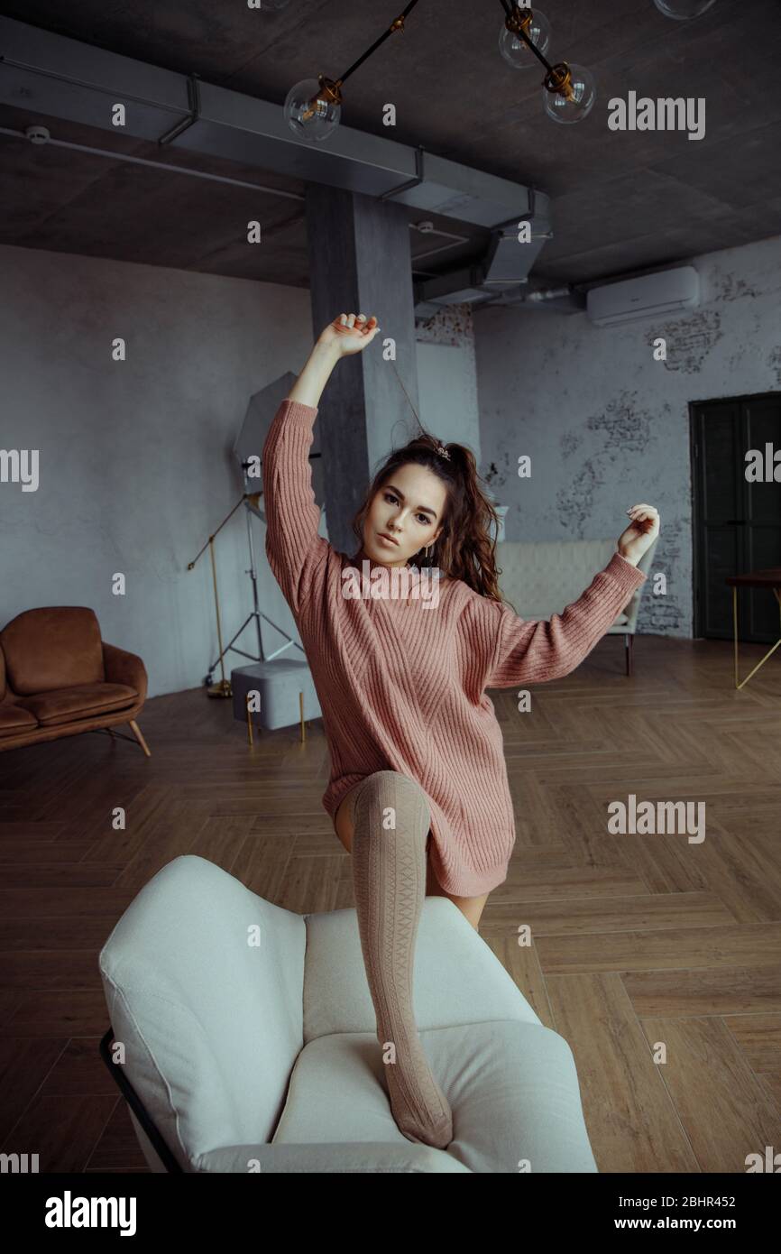 Una bella brunetta in un maglione rosa si posa nello Studio. La ragazza tocca i capelli, che si raccoglie in una coda di ponytail. Foto Stock