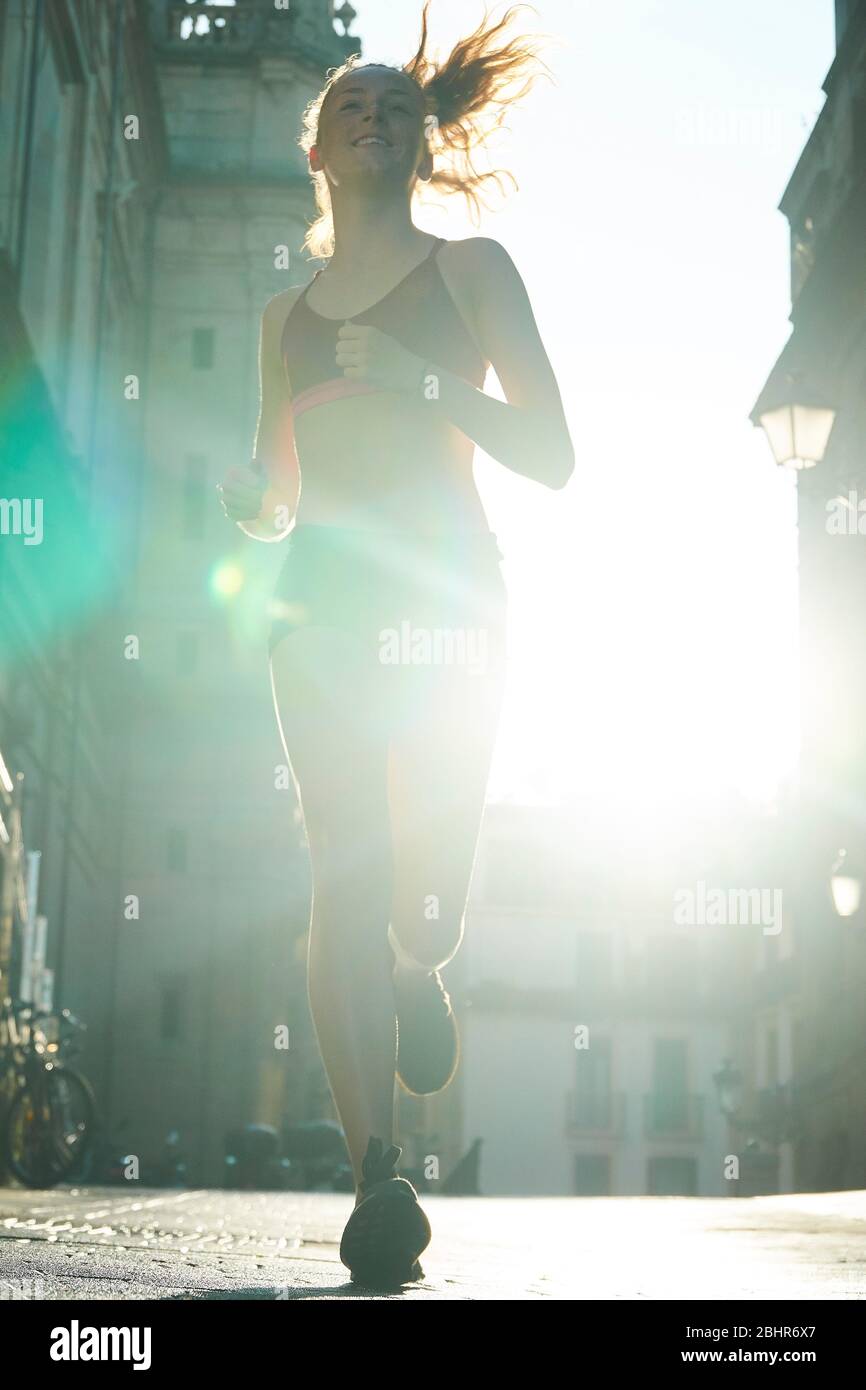una giovane donna che indossa abiti da corsa che corrono verso la  fotocamera con il sole dietro Foto stock - Alamy
