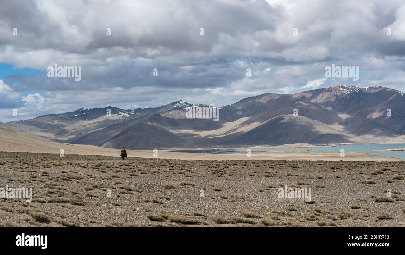 Lago di Karakul, Tagikistan - 27 giugno 2019: Shepperd su asino nel deserto al lago di Karakul con vista sulle alte montagne innevate e la valle, Tagikist Foto Stock