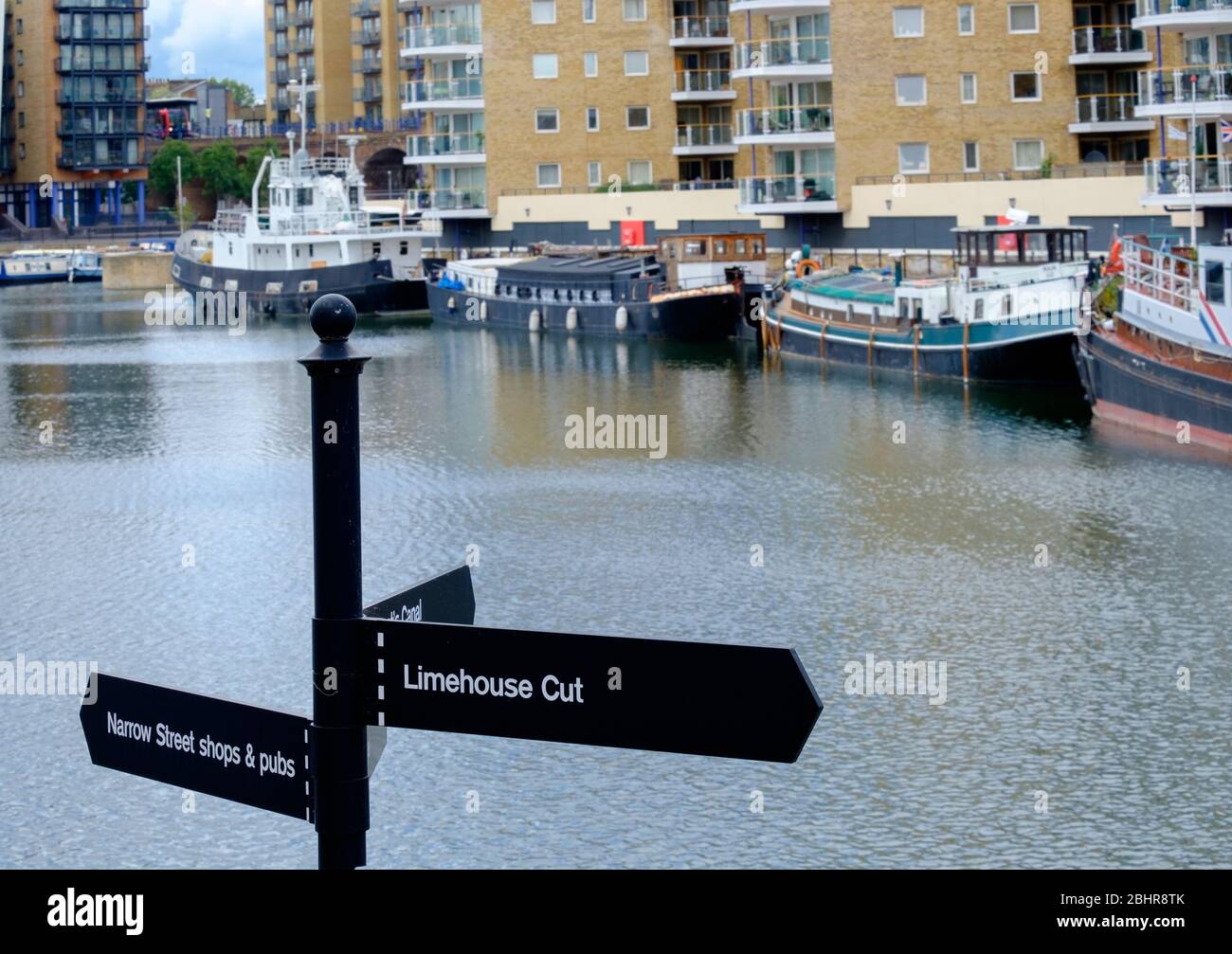 Cartello per Limehouse Cut & Narrow Street Shops & Pub con barche ormeggiate e alta riser residenziali sullo sfondo a Limehouse Marina, East London, UK Foto Stock