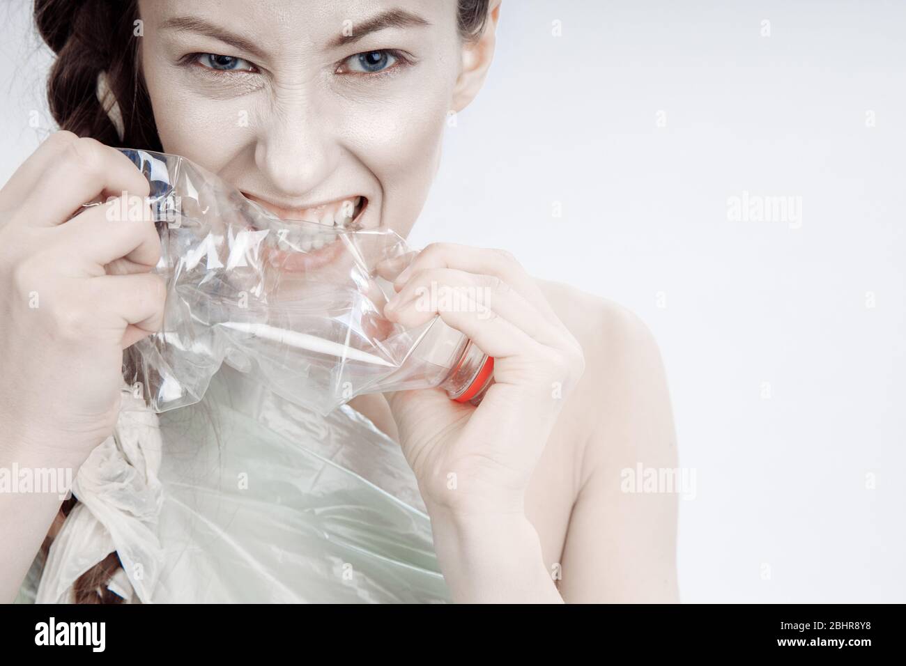 La ragazza cerca di rompere la bottiglia di plastica con i denti e le mani. Il genere della ragazza si preoccupa aggressivamente dei suoi denti. Foto Stock