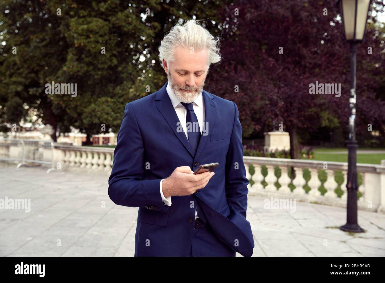 Un uomo che indossa un vestito e la cravatta in piedi in un passaggio pedonale guardando un telefono cellulare. Foto Stock