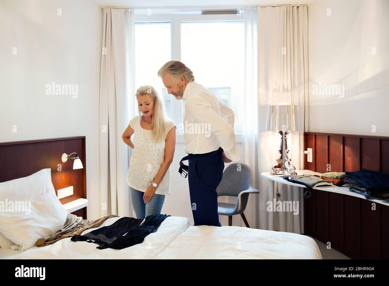 Una coppia in piedi in una camera d'albergo che guarda i vestiti disposti sul letto. Foto Stock