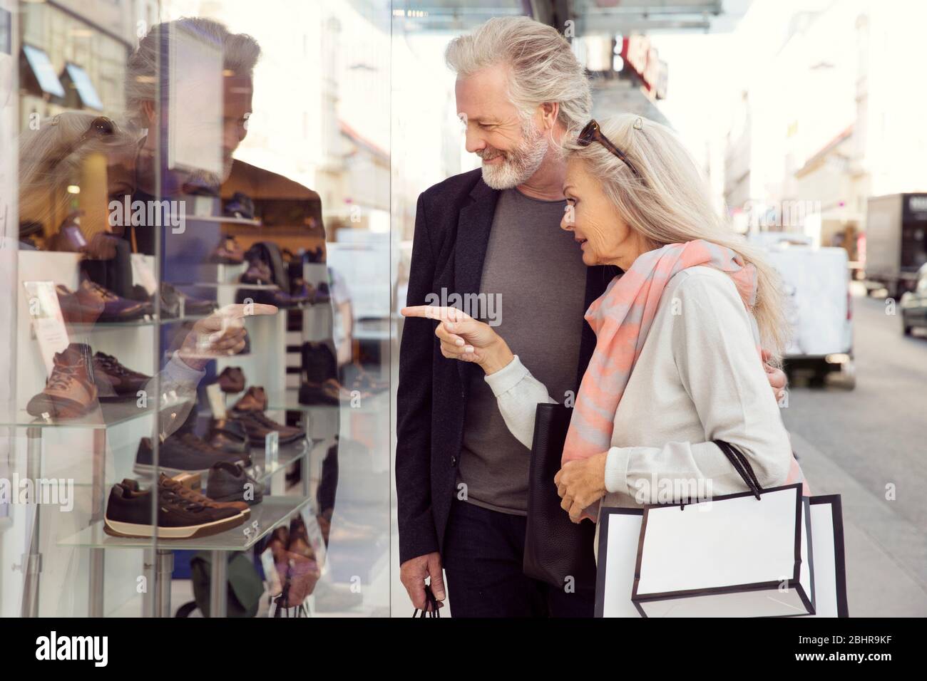 Una coppia con le braccia intorno l'un l'altro che trasporta le borse di shopping e che osserva in una finestra del negozio. Foto Stock