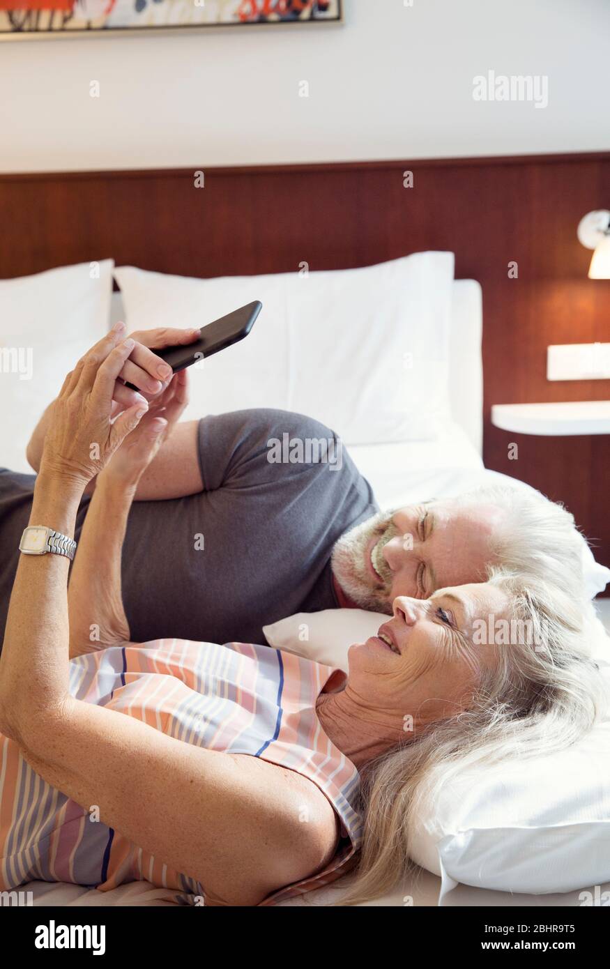 Una coppia sdraiata su un letto che guarda un telefono cellulare. Foto Stock